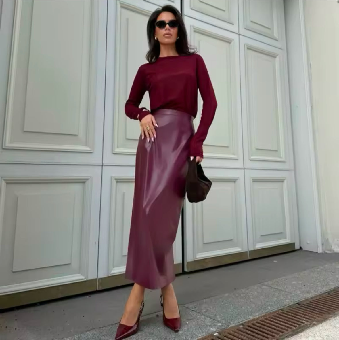 Eine stilvolle Frau trägt einen eleganten bordeauxfarbenen Midirock aus veganem Leder, kombiniert mit einem passenden Oberteil und Accessoires für einen zeitlosen, schicken Look.