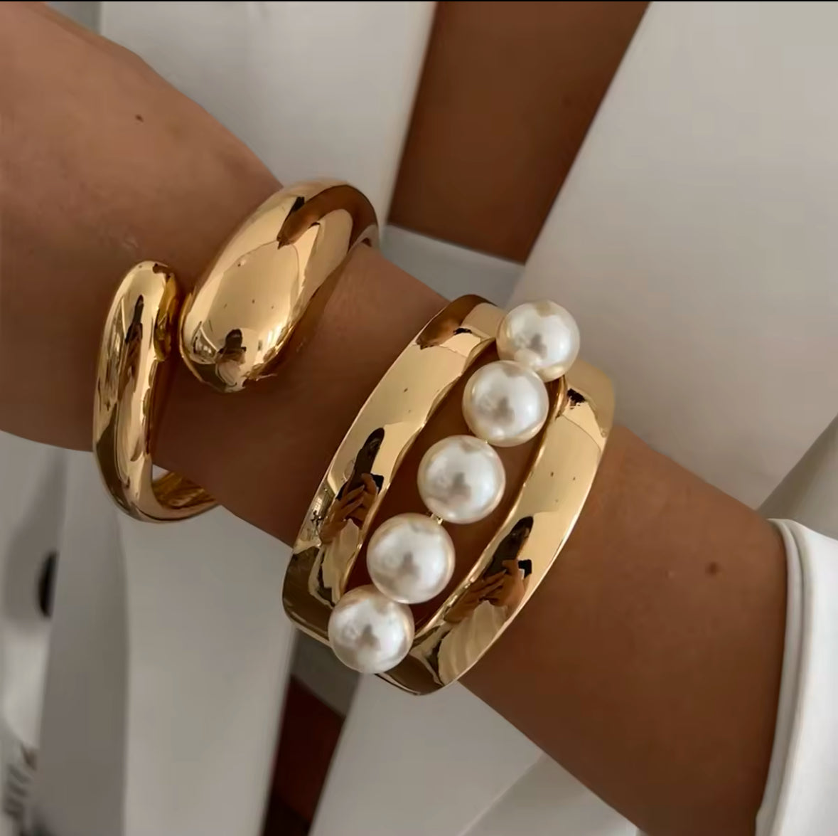 Goldene Statement-Armreifen mit skulpturaler Form und edlen Perlen-Details. Hochglanzpolierte Oberfläche für einen luxuriösen und modernen Look. Perfektes Accessoire für elegante Outfits und besondere Anlässe.