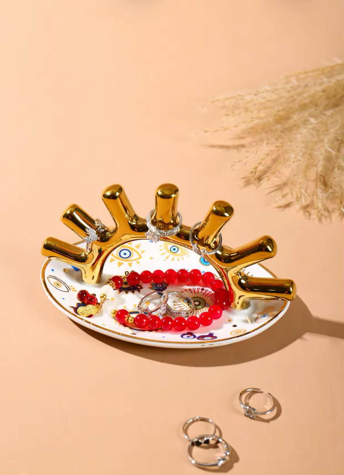 Goldener Schmuckhalter mit roten Perlenarmbändern und Ringen auf orientalischer Schale.
