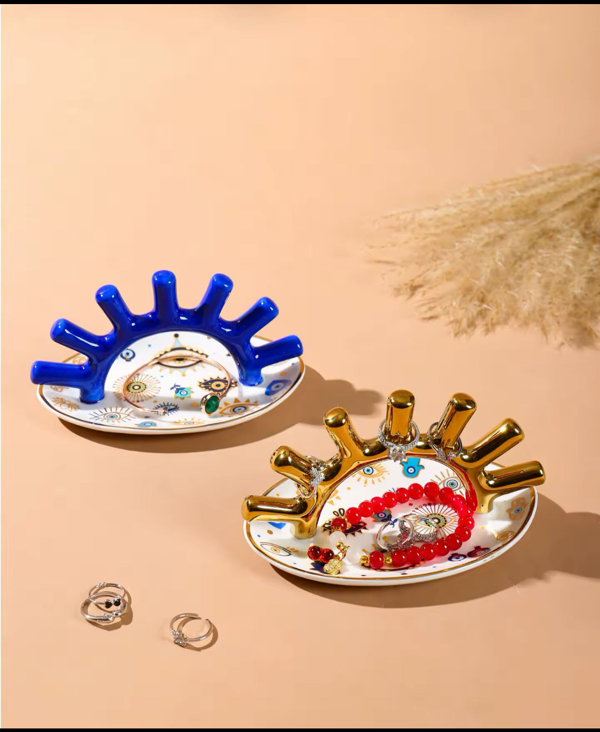 Zwei Schmuckhalter in Blau und Gold mit Evil-Eye-Design, dekoriert mit Ringen und Armbändern.