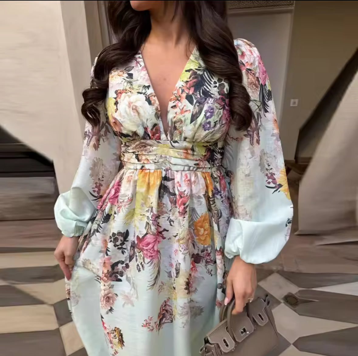 Frau trägt ein langes florales Maxikleid in Pastellfarben mit V-Ausschnitt und langen Ärmeln vor orientalischer Kulisse