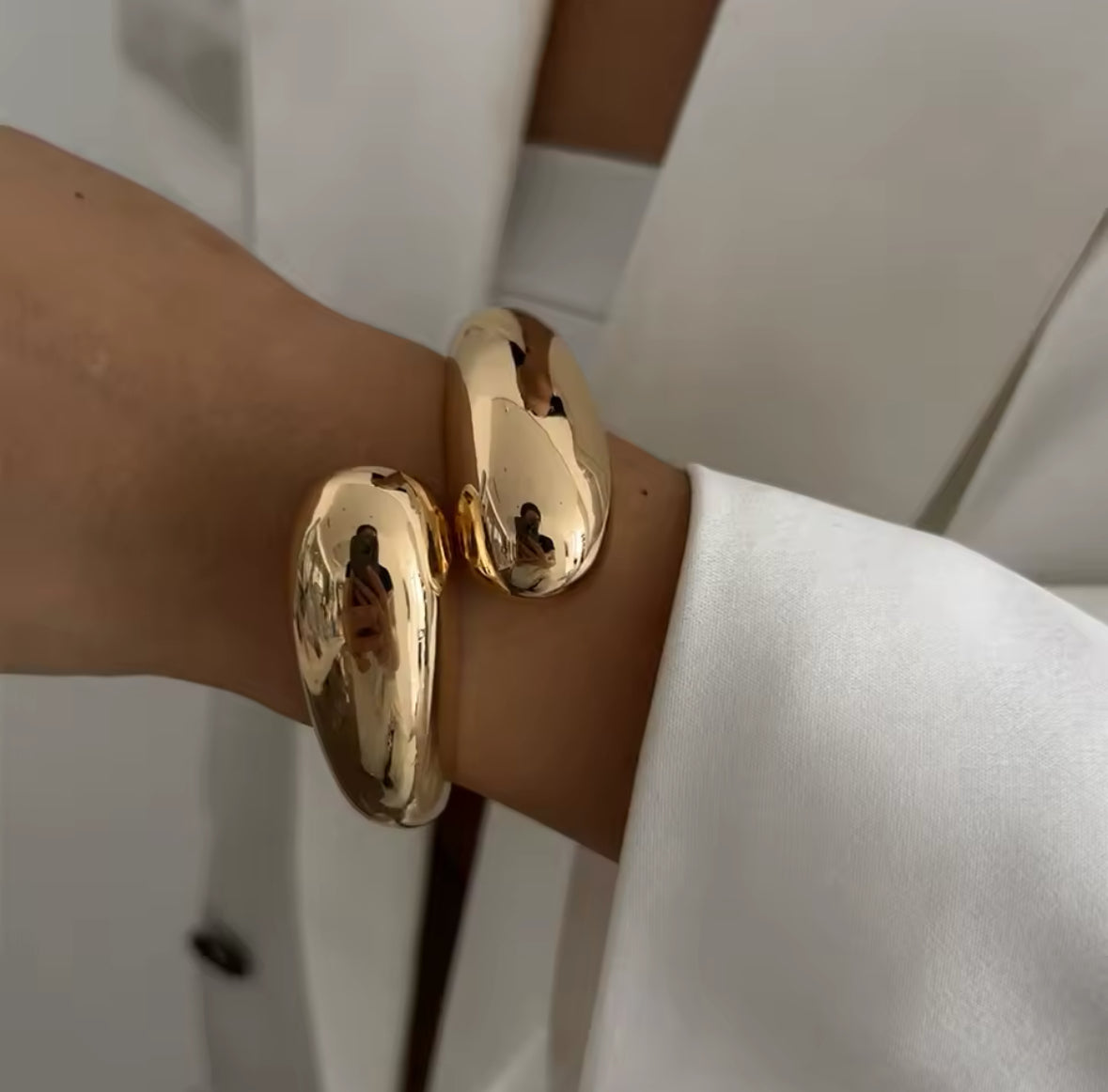 Massiver goldener Armreif mit organischer, geschwungener Form. Hochglänzende, luxuriöse Oberfläche für einen modernen und eleganten Look. Perfekt als Statement-Schmuckstück für minimalistische und stilvolle Outfits