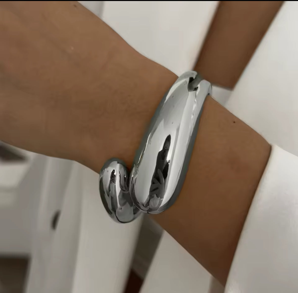 Statement-Armreifen in Silber und Silber mit skulpturalem, modernen Design. Ein Armband aus glänzendem Gold mit offenen Cut-Outs und Perlen-Akzent, das andere aus poliertem Silber mit einer organischen, geschwungenen Form. Luxuriöse Schmuckstücke für einen eleganten, avantgardistischen Look.