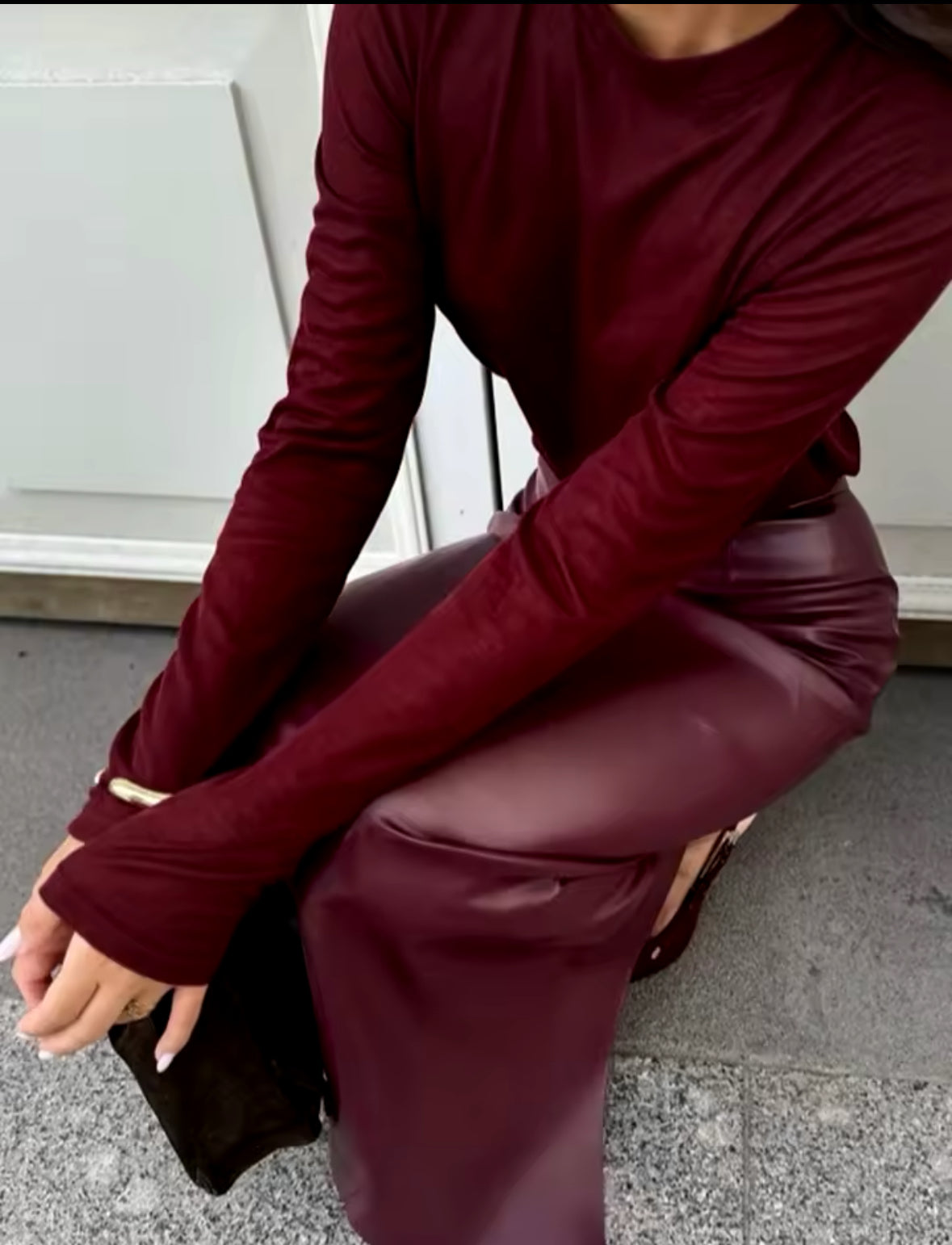 Eine stilvolle Frau trägt einen eleganten bordeauxfarbenen Midirock aus veganem Leder, kombiniert mit einem passenden Oberteil und Accessoires für einen zeitlosen, schicken Look.