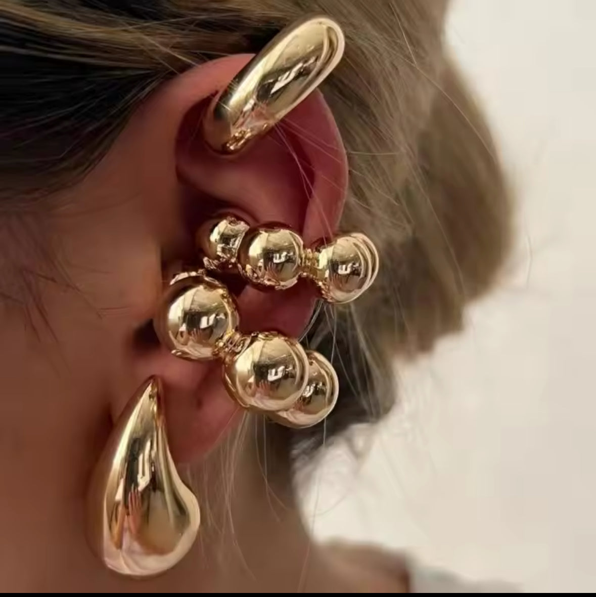 Nahaufnahme eines modernen, mehrteiligen Ear-Cuff-Ohrrings in glänzendem Gold. Das Design kombiniert runde Kugel-Elemente mit geschwungenen Formen, die sich elegant um das Ohr schmiegen. Der auffällige Schmuck verleiht einen futuristischen, luxuriösen Look.