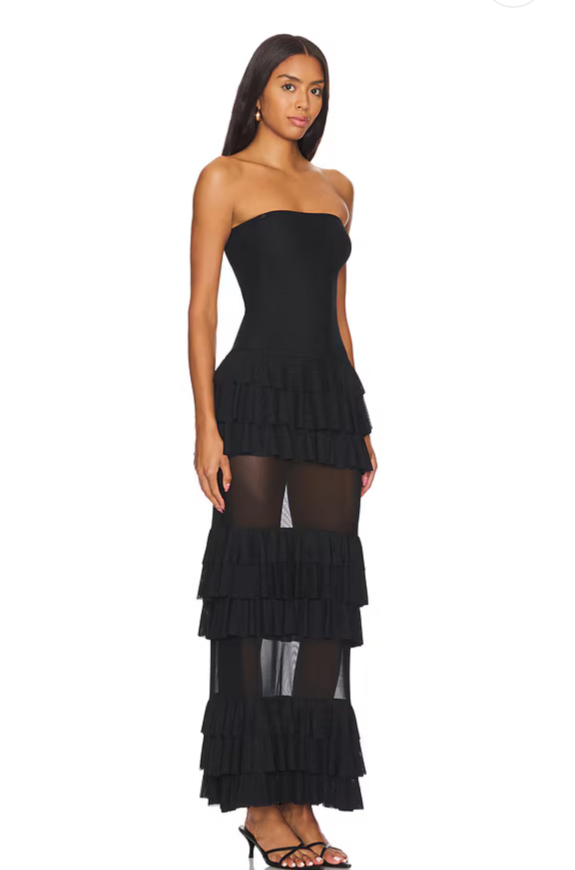 Model trägt ein trägerloses schwarzes Maxikleid mit mehreren Lagen Volants und transparenten Mesh-Einsätzen im Rockbereich. Das Kleid betont die Taille und wirkt elegant und feminin.