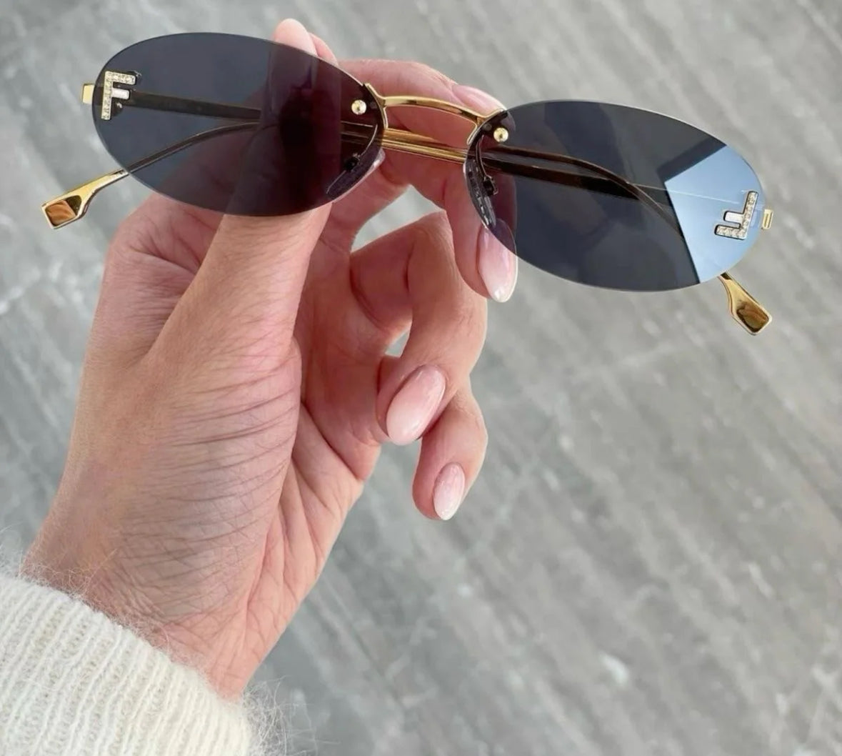F-Vibe Sonnenbrille mit Goldrahmen und F-Detail – flach fotografiert auf grauem Steinboden