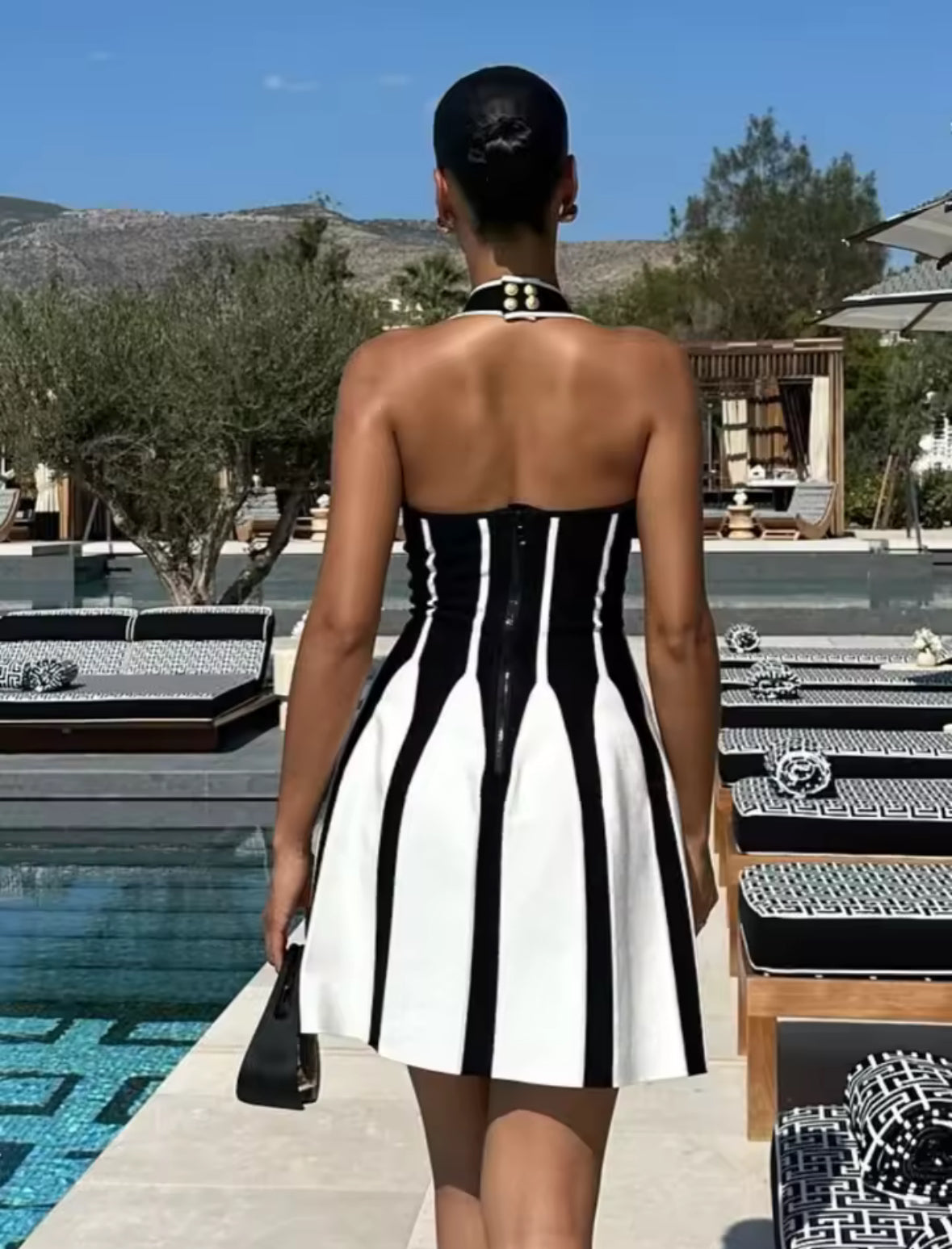 Modell trägt ein schwarz-weißes Kleid im architektonischen Look mit V-Ausschnitt, breiten Trägern und ausgestelltem Rock. Die Figur wird durch das Linien-Design optisch betont.
