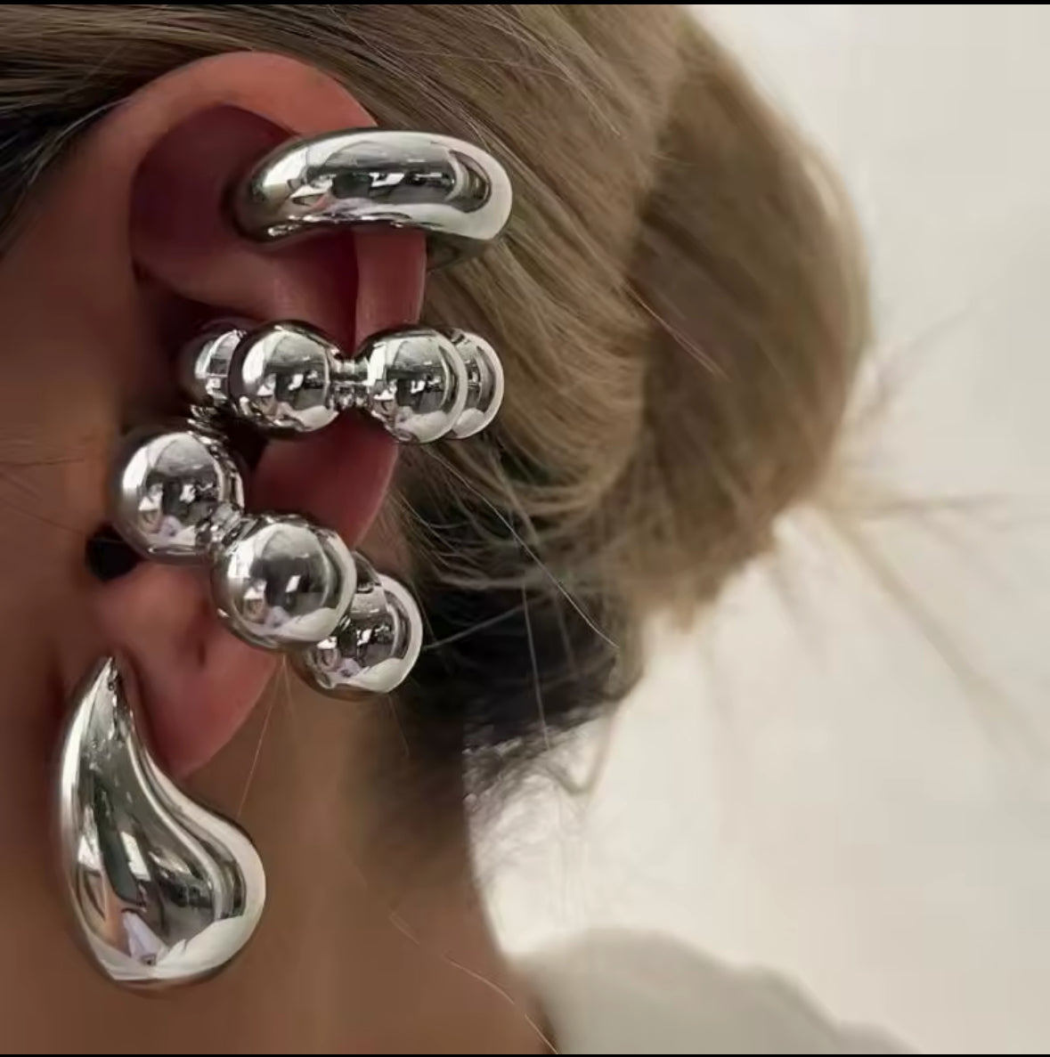 Nahaufnahme eines futuristischen Ear-Cuff-Ohrrings in glänzendem Silber. Das Design besteht aus mehreren Kugel- und Tropfen-Elementen, die kunstvoll das gesamte Ohr umschließen. Die hochglänzende Oberfläche reflektiert das Licht und sorgt für einen modernen, avantgardistischen Stil.