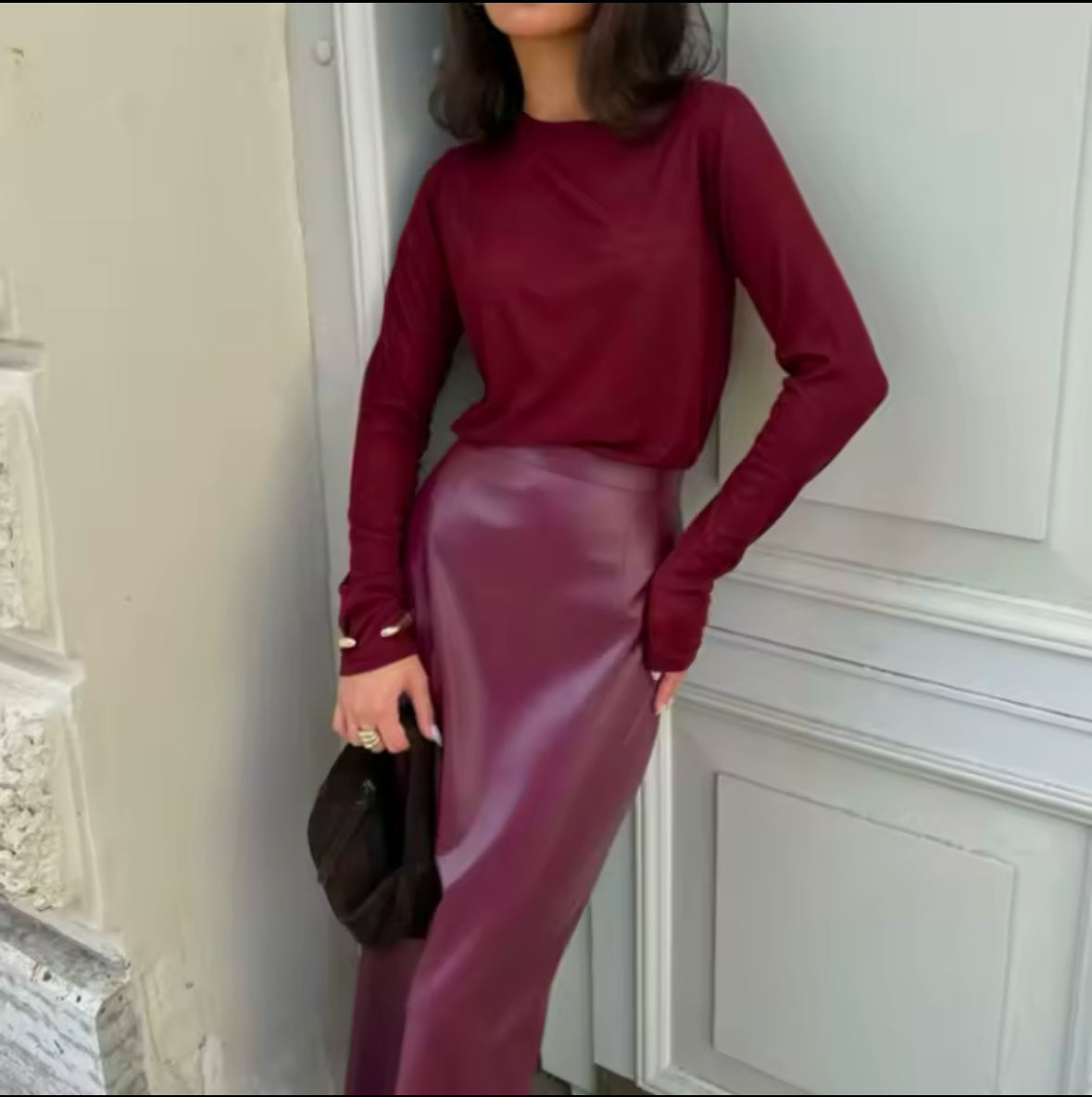 Eine stilvolle Frau trägt einen eleganten bordeauxfarbenen Midirock aus veganem Leder, kombiniert mit einem passenden Oberteil und Accessoires für einen zeitlosen, schicken Look.