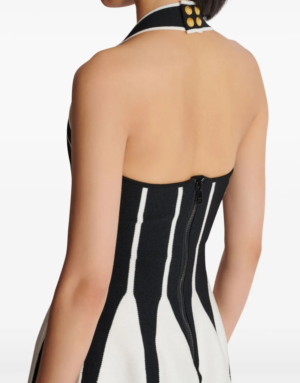 Modell trägt ein schwarz-weißes Kleid im architektonischen Look mit V-Ausschnitt, breiten Trägern und ausgestelltem Rock. Die Figur wird durch das Linien-Design optisch betont.