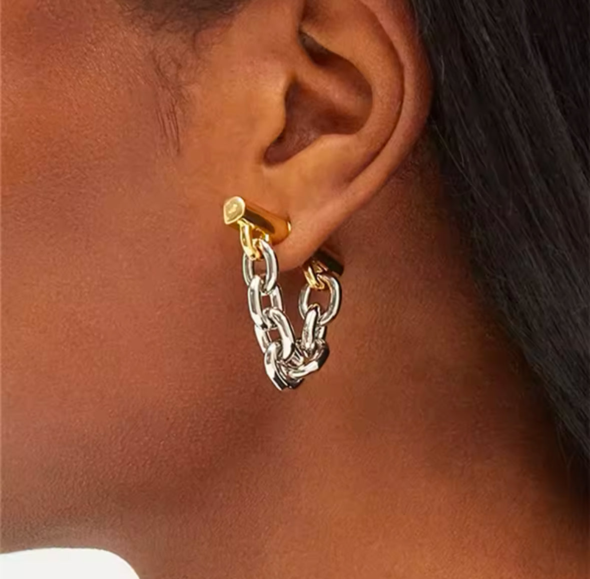 Nahaufnahme eines stilvollen Ohrrings mit Kettendesign in Bicolor-Optik. Der Ohrring besteht aus einer Mischung aus gold- und silberfarbenen Gliedern, die an einer goldfarbenen Befestigung am Ohr befestigt sind. Der Schmuck verleiht einen modernen, edgy Look mit einem Hauch von Luxus.