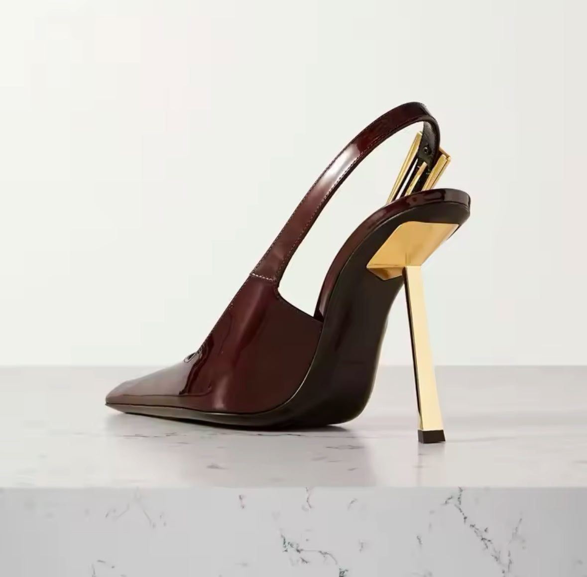 Luxuriöser burgundy-roter Lackleder-Slingback-Pumps mit spitzer Zehenpartie und glänzendem Finish. Der Schuh hat einen schmalen, goldfarbenen Absatz und ein auffälliges geometrisches Metallelement an der Ferse, das für einen modernen und edlen Look sorgt. Perfekt für elegante Outfits mit einem Hauch von Extravaganz.