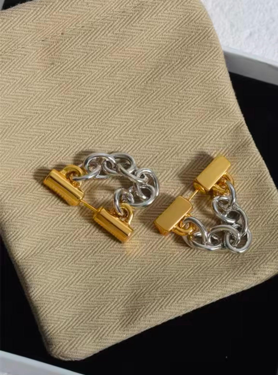 Nahaufnahme eines stilvollen Ohrrings mit Kettendesign in Bicolor-Optik. Der Ohrring besteht aus einer Mischung aus gold- und silberfarbenen Gliedern, die an einer goldfarbenen Befestigung am Ohr befestigt sind. Der Schmuck verleiht einen modernen, edgy Look mit einem Hauch von Luxus.