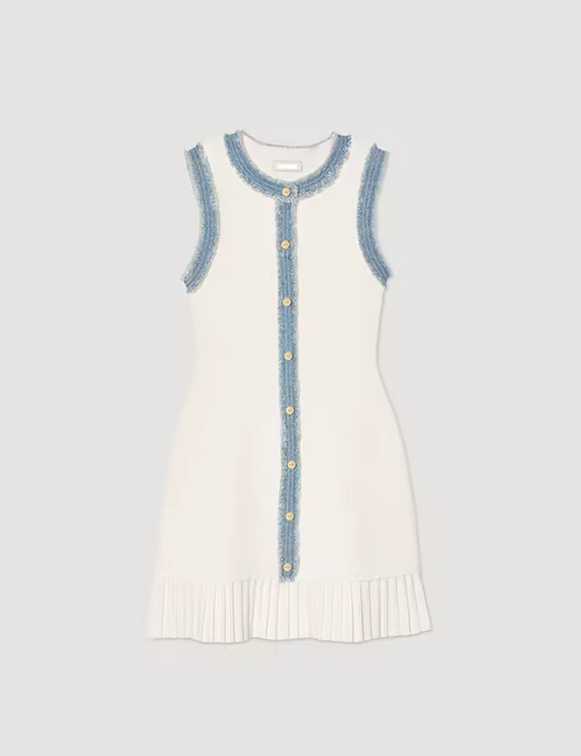 Ärmelloses, cremeweißes Minikleid mit goldener Knopfleiste, blauen Fransen-Details und plissiertem Saum – elegant gestylt mit Tasche und Heels, aufgenommen vor einem verspiegelten Interior.