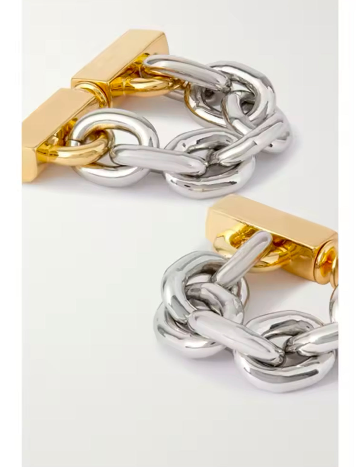 Nahaufnahme eines stilvollen Ohrrings mit Kettendesign in Bicolor-Optik. Der Ohrring besteht aus einer Mischung aus gold- und silberfarbenen Gliedern, die an einer goldfarbenen Befestigung am Ohr befestigt sind. Der Schmuck verleiht einen modernen, edgy Look mit einem Hauch von Luxus.