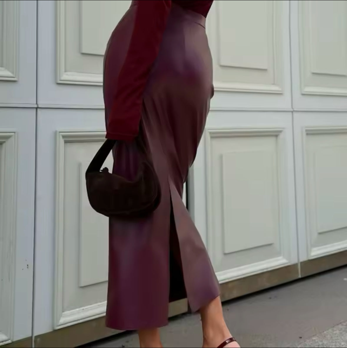 Eine stilvolle Frau trägt einen eleganten bordeauxfarbenen Midirock aus veganem Leder, kombiniert mit einem passenden Oberteil und Accessoires für einen zeitlosen, schicken Look.