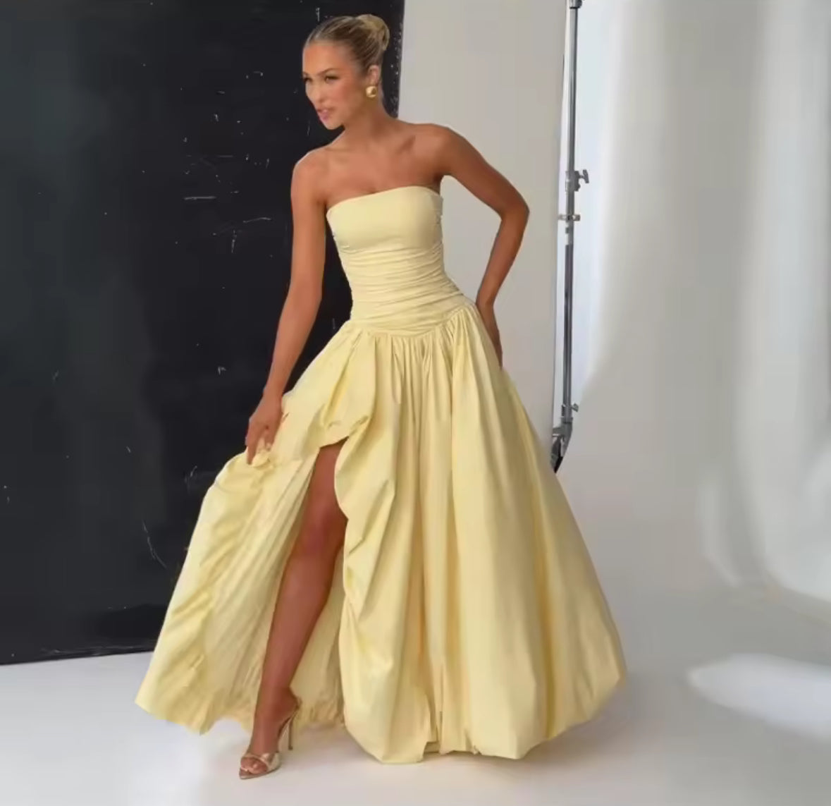 Model trägt trägerloses gelbes High-Low-Kleid mit Schlitz vorne
