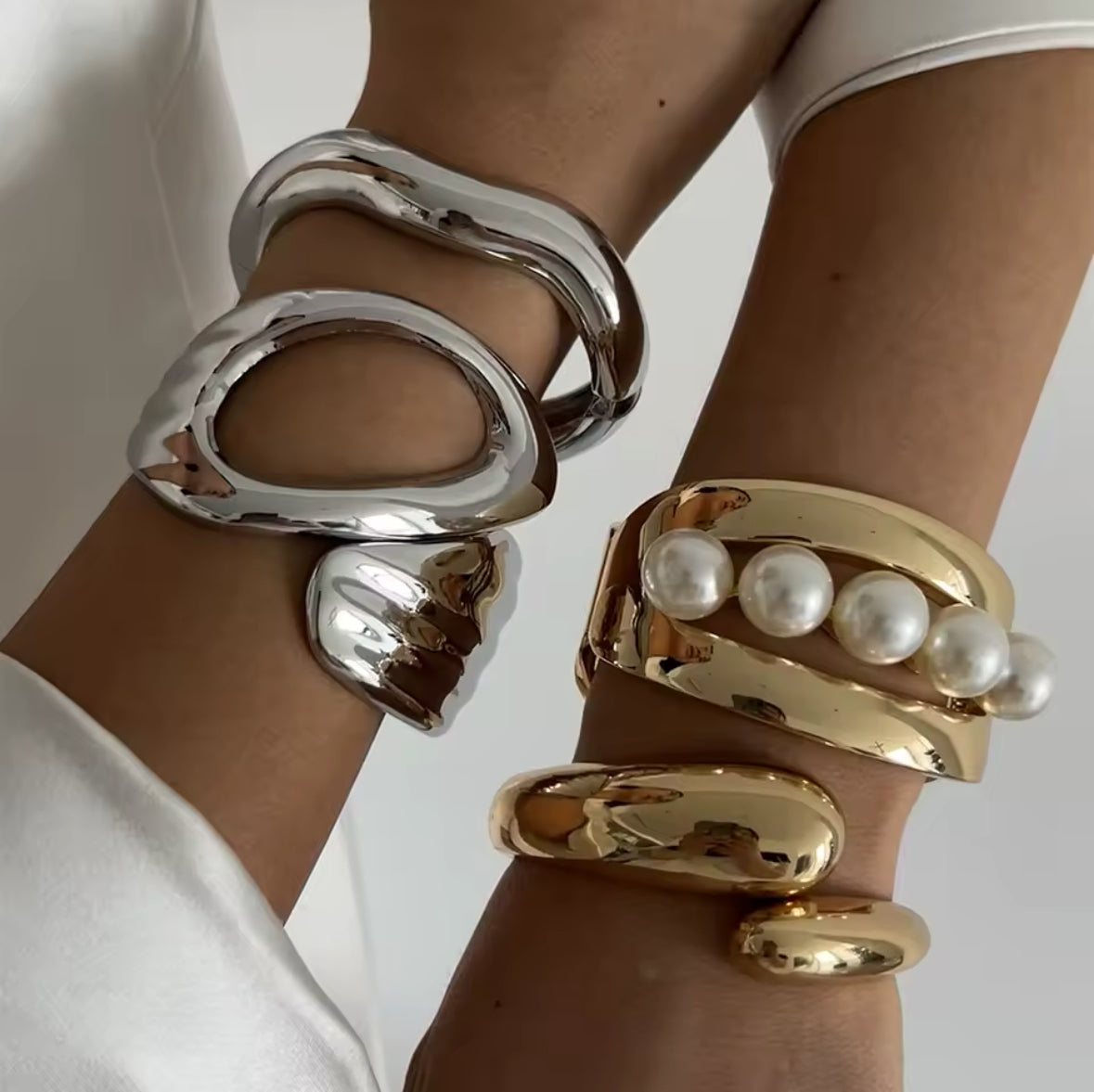 mit skulpturalem, modernen Design. Ein Armband aus glänzendem Gold mit offenen Cut-Outs und Perlen-Akzent, das andere aus poliertem Silber mit einer organischen, geschwungenen Form. Luxuriöse Schmuckstücke für einen eleganten, avantgardistischen Look.