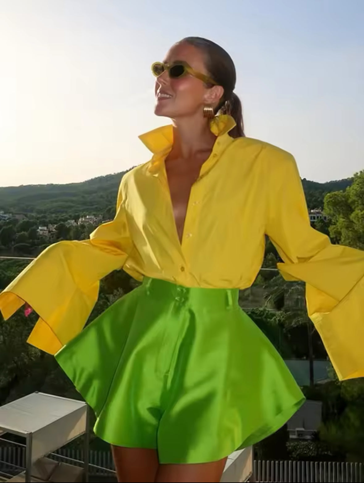 grüne Satin-Shorts mit High-Waist-Design, kombiniert mit einer auffälligen gelben Bluse und Statement-Ohrringen für einen sommerlichen Trend-Look.