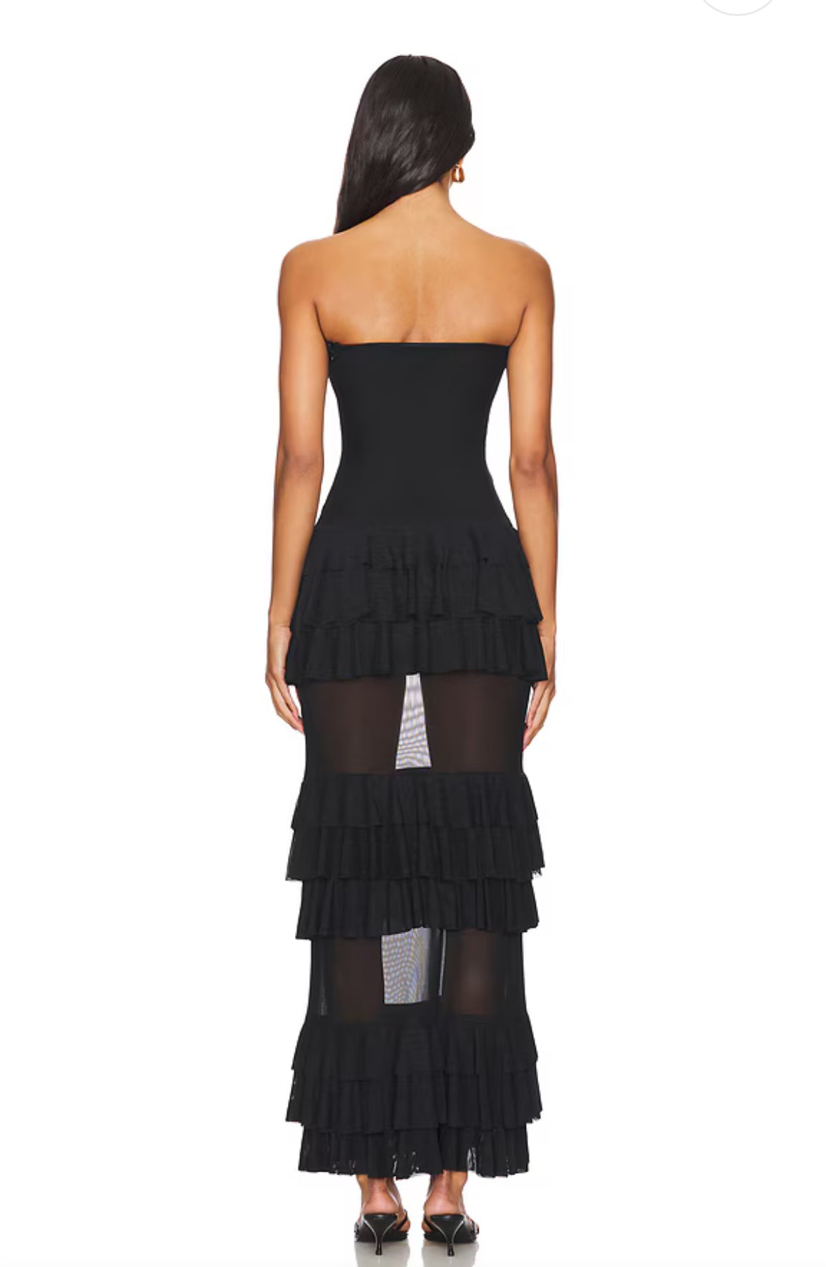 Model trägt ein trägerloses schwarzes Maxikleid mit mehreren Lagen Volants und transparenten Mesh-Einsätzen im Rockbereich. Das Kleid betont die Taille und wirkt elegant und feminin.