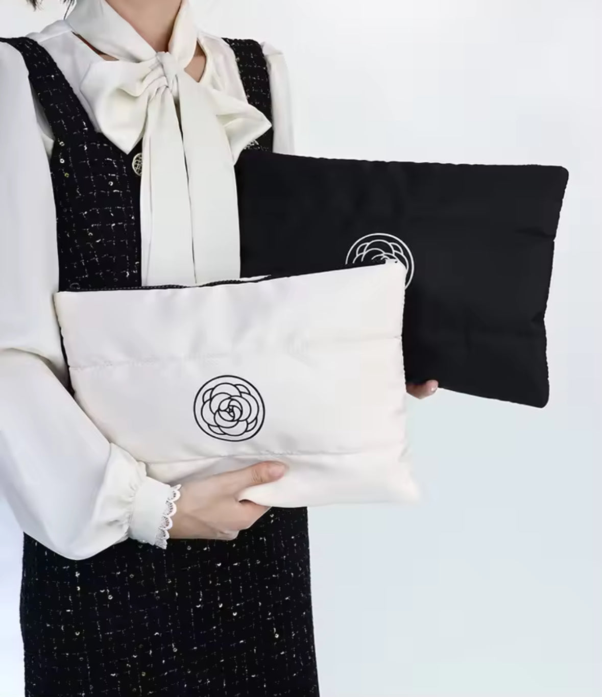 Zwei stilvolle Kosmetiktaschen in Schwarz und Creme mit wattierter Oberfläche und einem minimalistischen Rosen-Logo. Perfekt für die Aufbewahrung von Make-up und Pflegeprodukten unterwegs.