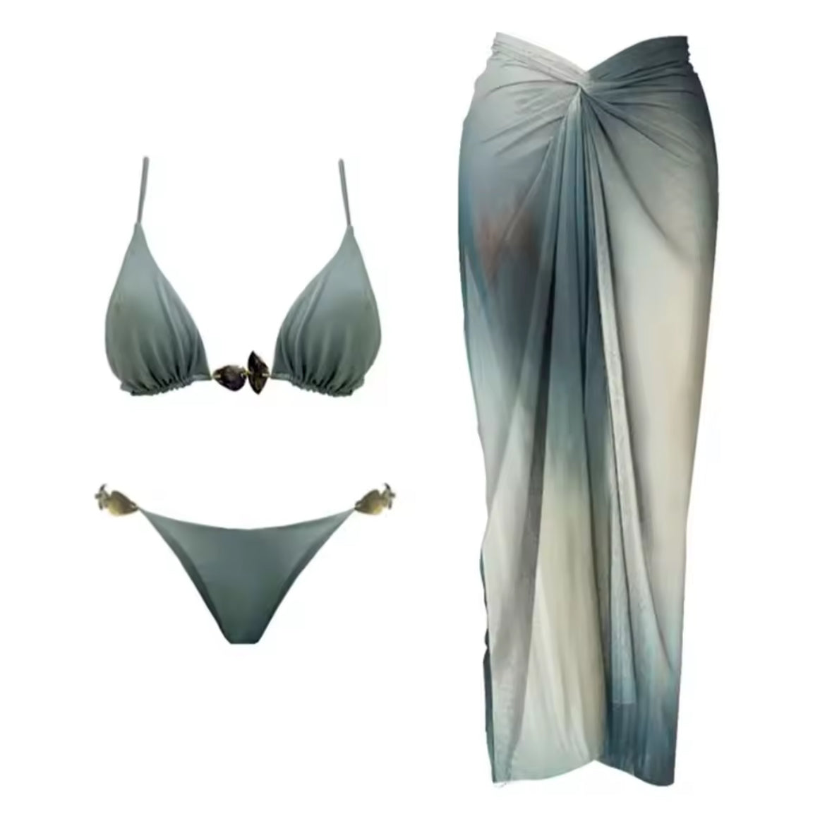 Frau trägt ein dreiteiliges Bikini-Set in Meeresfarben mit Muscheldetails und transparentem Sarong vor Steinwand.
