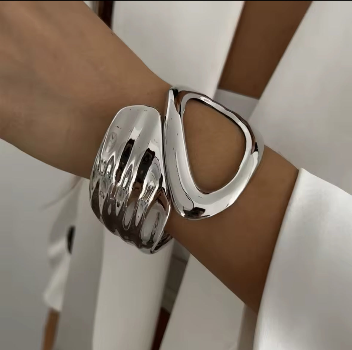 Skulpturaler silberner Armreif mit modernem Cut-Out-Design und geschwungener Form. Hochglanzpolierte Oberfläche für einen avantgardistischen und eleganten Look. Ein einzigartiges Statement-Schmuckstück für minimalistische und stilvolle Outfits.