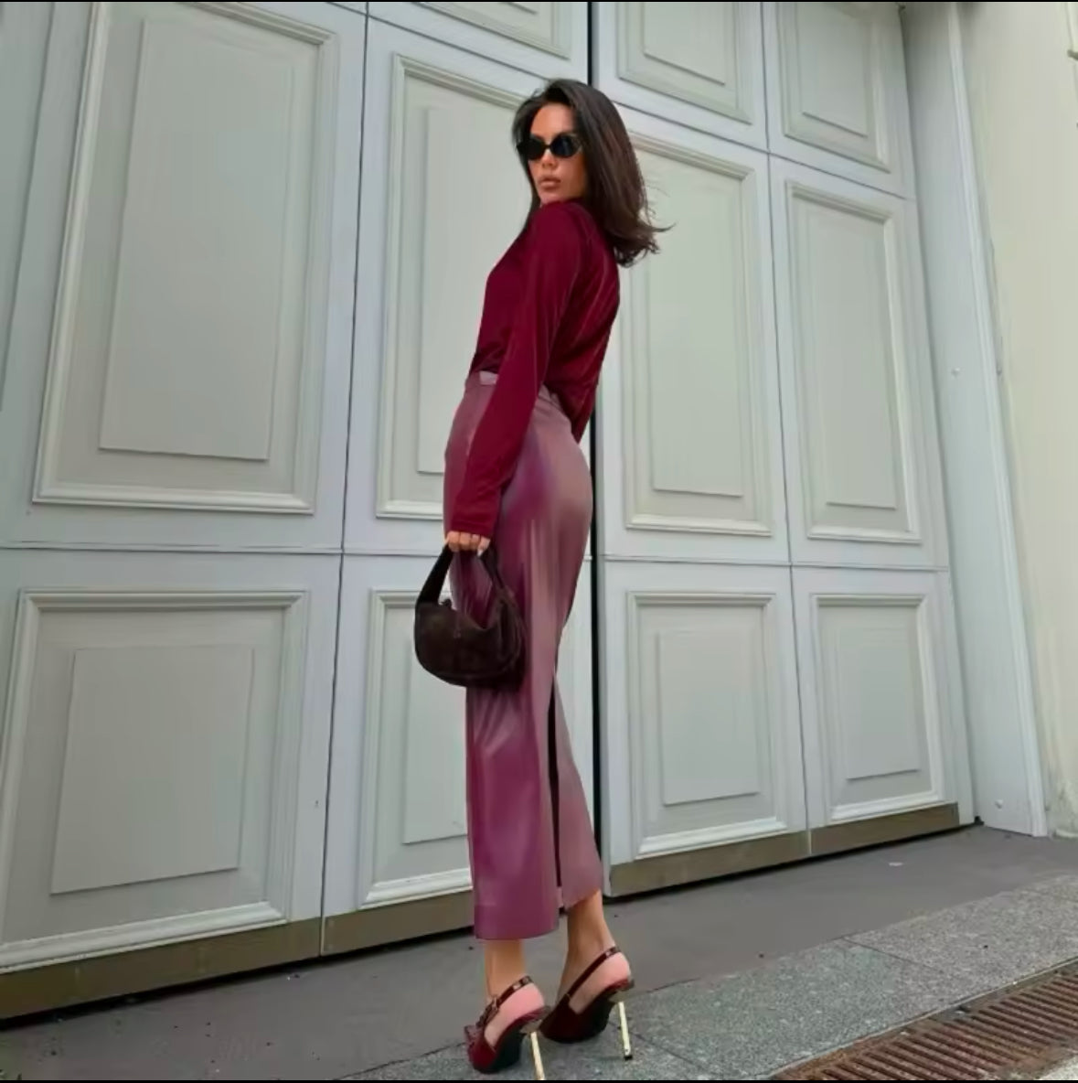 Eine stilvolle Frau trägt einen eleganten bordeauxfarbenen Midirock aus veganem Leder, kombiniert mit einem passenden Oberteil und Accessoires für einen zeitlosen, schicken Look.