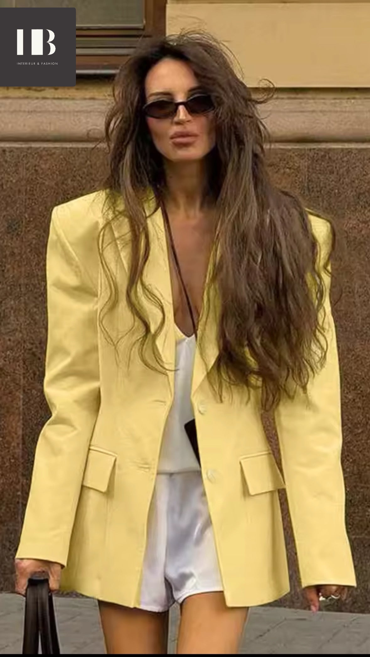 Frau trägt einen zitronengelben, oversized geschnittenen Blazer mit markanten Schultern und langen Ärmeln. Der Look wirkt modern, stark und sommerlich elegant.