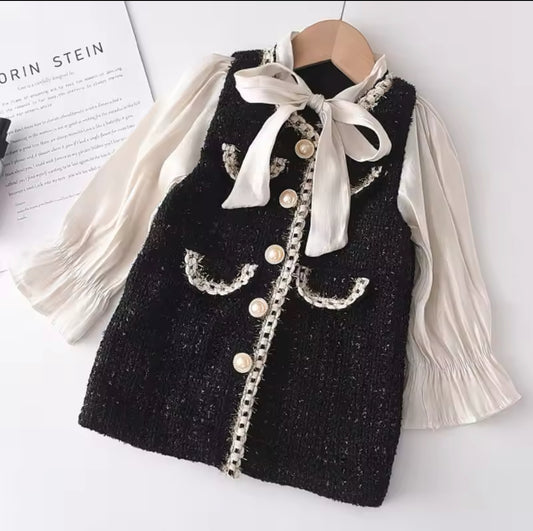 Mädchen-Tweed-Kleid in Schwarz mit Perlenknöpfen, dekorativen Taschen und cremefarbener Bluse mit Schleife und langen Ärmeln.