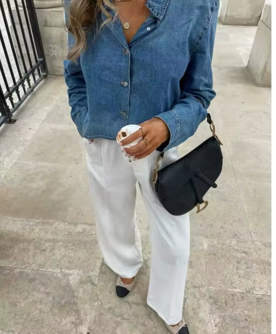 Modische cropped Jeansbluse mit langen Ärmeln, vorne geschlossen mit Knopfleiste, hinten komplett rückenfrei mit Bindeband – getragen mit weißer High-Waist-Hose im Pariser Innenhof.