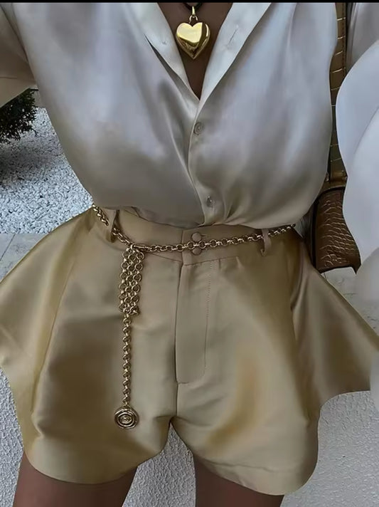 Elegante champagner Satin-Shorts mit High-Waist-Passform, kombiniert mit einer fließenden Seidenbluse und goldenen Accessoires für einen luxuriösen Look.