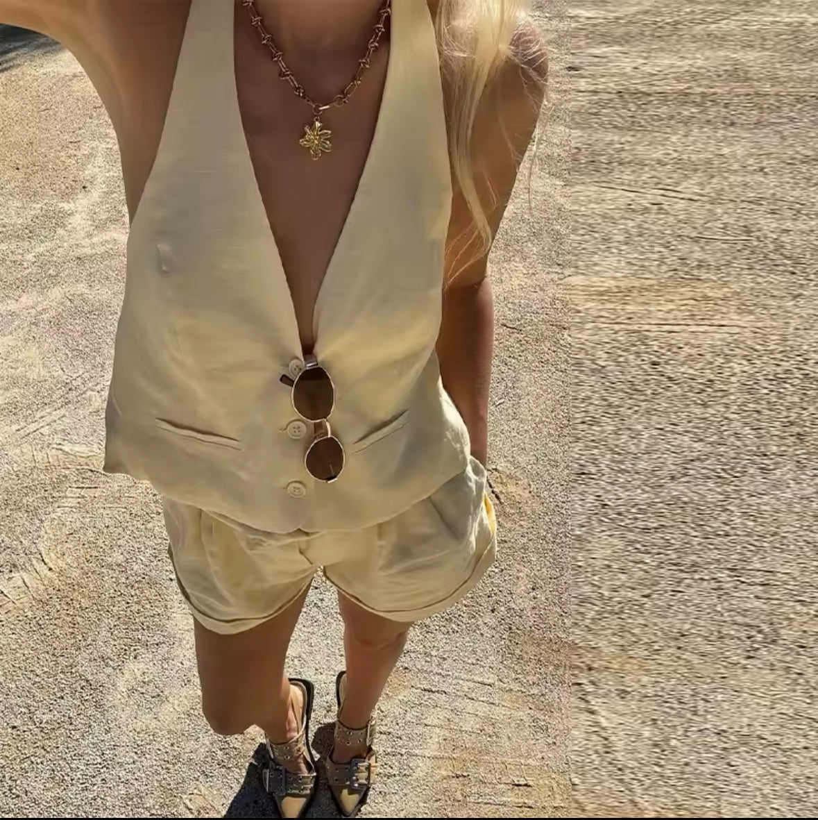 Frau trägt ein zweiteiliges Sommer-Set aus hellgelbem Leinen bestehend aus tief ausgeschnittener Neckholder-Weste und High-Waist-Shorts. Das Outfit wirkt luftig, modern und sommerlich elegant – ideal für warme Tage in der Stadt oder im Urlaub.