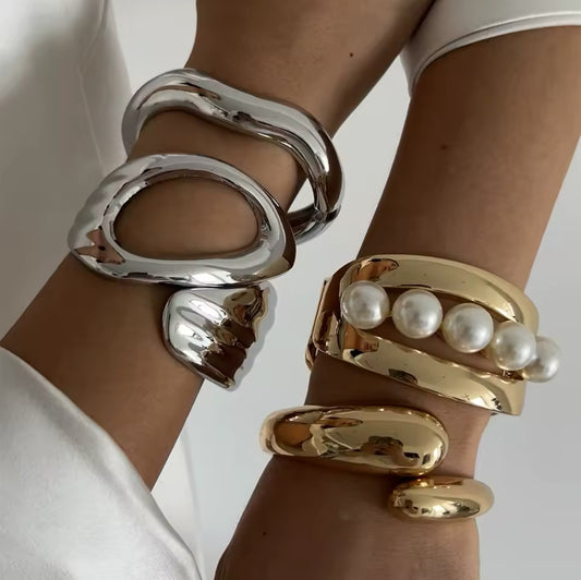 mit skulpturalem, modernen Design. Ein Armband aus glänzendem Gold mit offenen Cut-Outs und Perlen-Akzent, das andere aus poliertem Silber mit einer organischen, geschwungenen Form. Luxuriöse Schmuckstücke für einen eleganten, avantgardistischen Look.