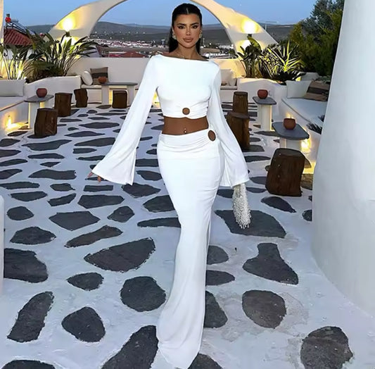 Frau in einem weißen, figurbetonten Set mit goldenen Cut-Out-Details, stehend auf einer mediterranen Terrasse
