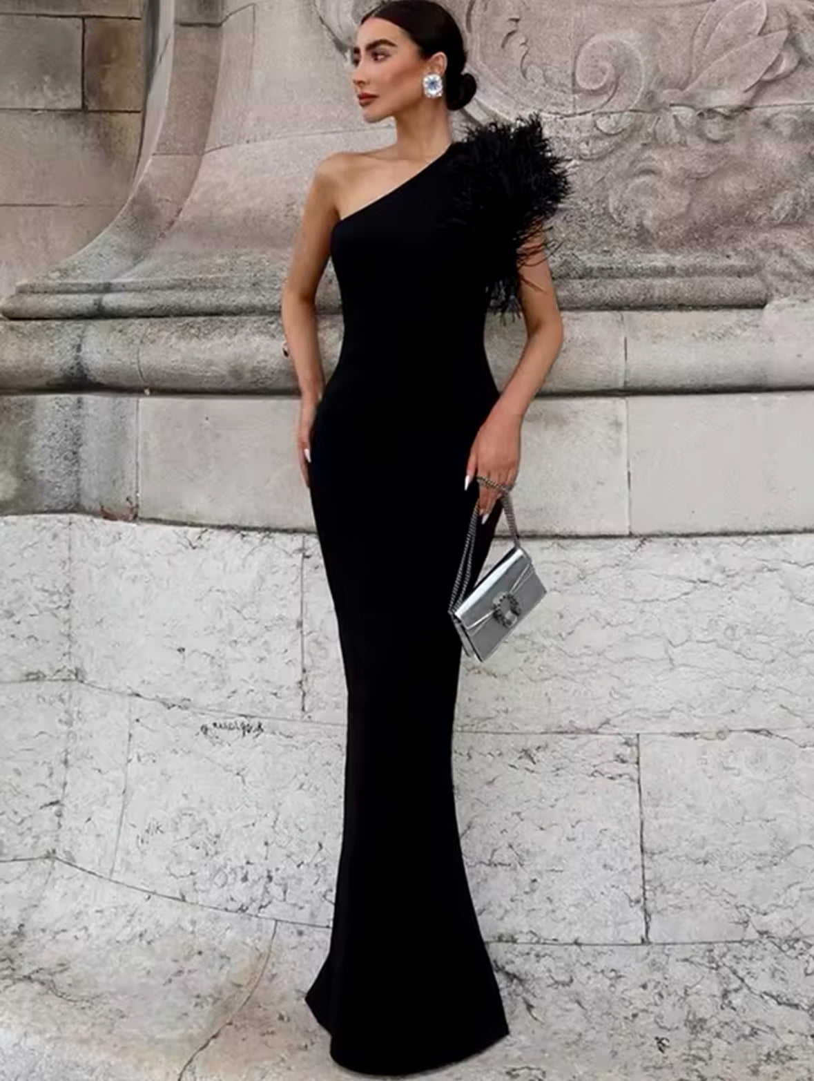 Schwarzes, bodenlanges Abendkleid mit asymmetrischem One-Shoulder-Schnitt und schwarzem Federbesatz an der Schulter – getragen vor Pariser Kulisse mit Eiffelturm im Hintergrund.
