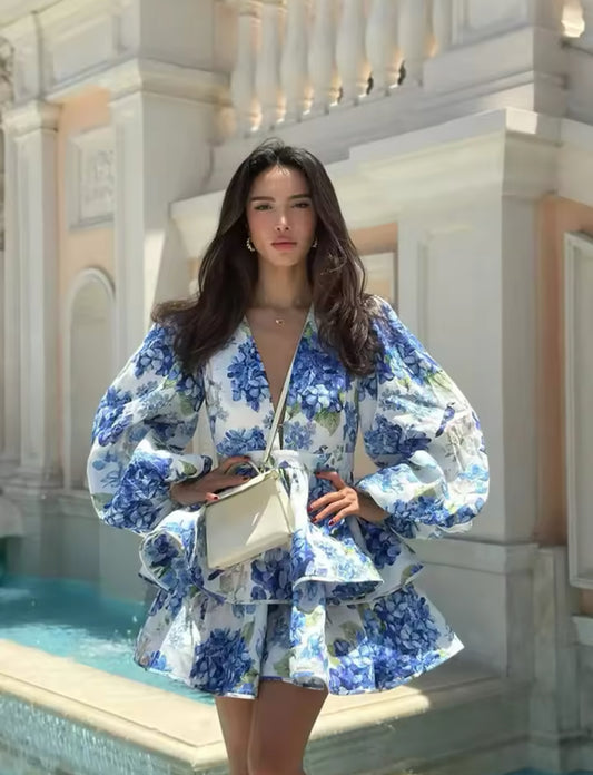 Weißes Minikleid mit blauem Blumenprint, voluminösen Puffärmeln und Rüschenrock – eleganter mediterraner Look.