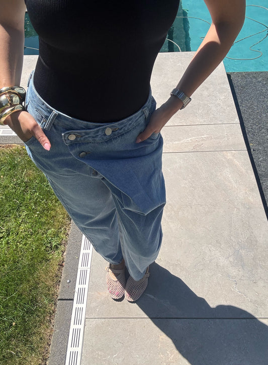 Frau trägt eine locker sitzende, crossover-geschnittene Oversized Jeans in Hellblau, kombiniert mit einem schwarzen Neckholder-Body. Die Jeans hat einen auffälligen Bund und einen coolen Streetstyle-Look.